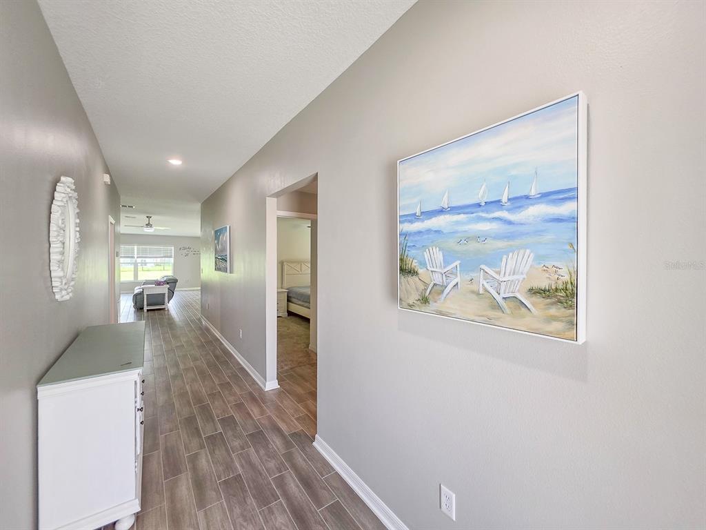 A hallway with wood-look tile flooring leads to a living area past a bedroom doorway — 207 WINGED FOOT LANE, DAYTONA BEACH, FL