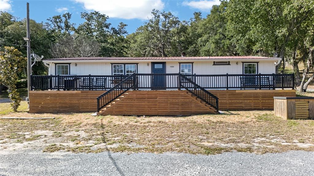 A single-story house with a large wooden deck and black railings sits among trees — 14318 ROCK N ROLL ROAD, CLERMONT, FL