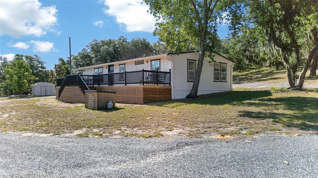 A white manufactured home features a large wooden deck with black railings and stairs — 14318 ROCK N ROLL ROAD, CLERMONT, FL