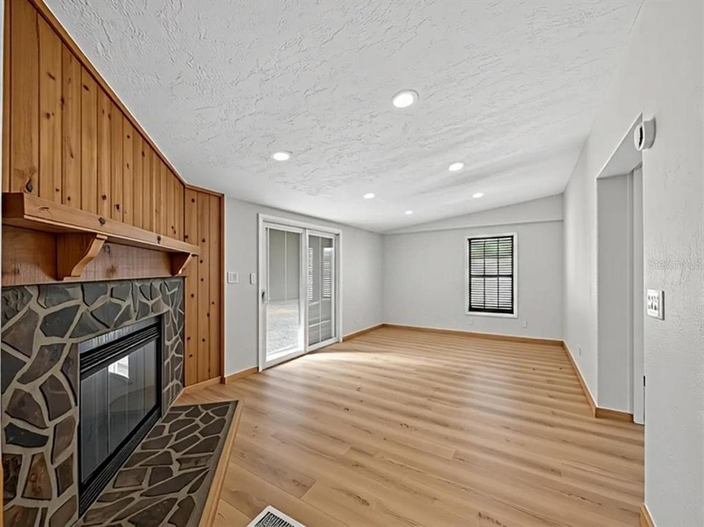 A living room features light wood flooring, a stone fireplace with wood paneling, and sliding doors — 14318 ROCK N ROLL ROAD, CLERMONT, FL