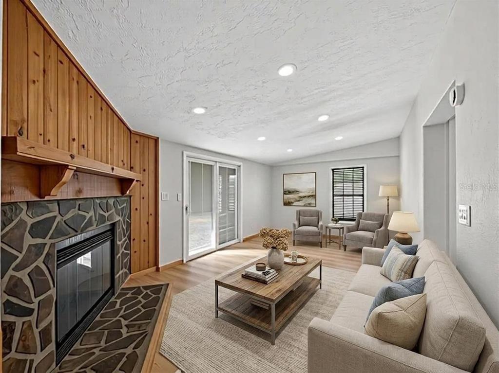 A living room features a stone fireplace, wood paneling, sliding glass doors, and neutral furniture — 14318 ROCK N ROLL ROAD, CLERMONT, FL