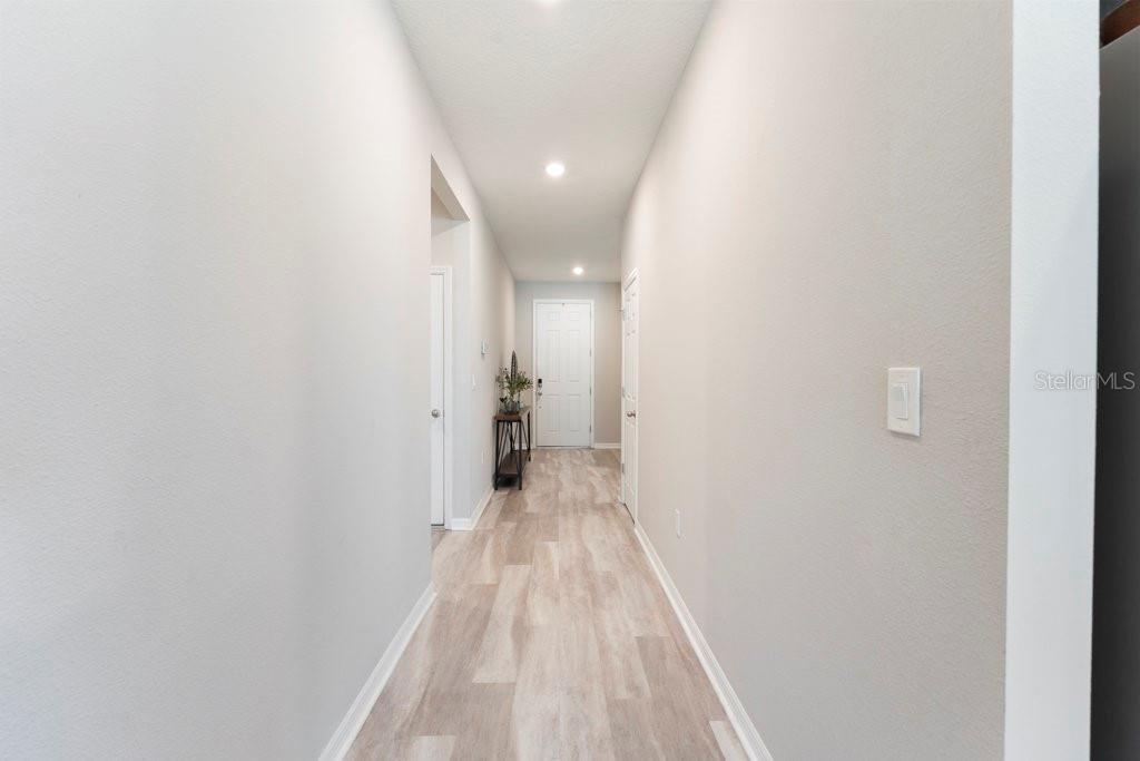 A hallway features light wood-look flooring, white walls, recessed lighting, and a white entry door — 245 MESSINA PLACE, HOWEY IN THE HILLS, FL