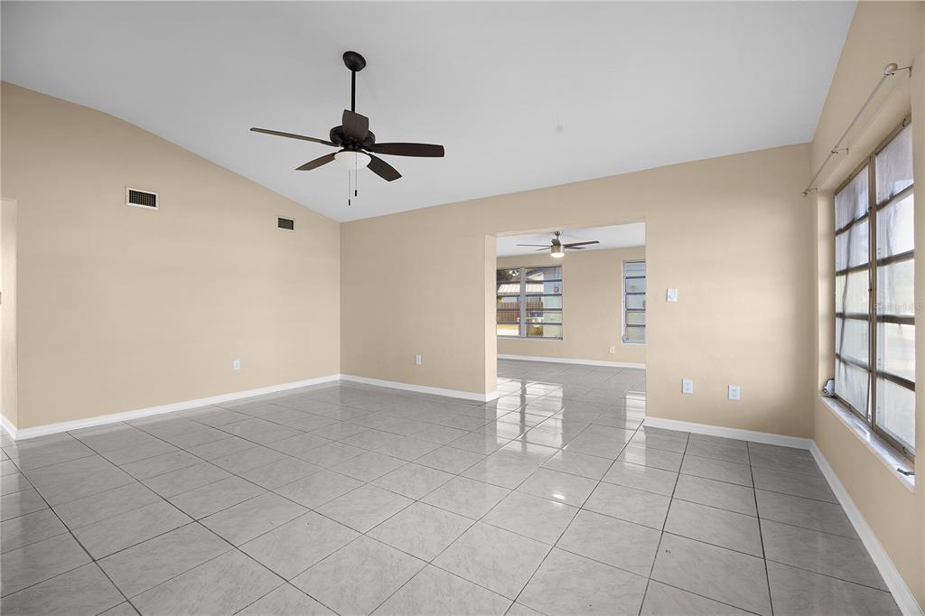 An empty living room features light-colored tile flooring, beige walls, and a vaulted ceiling — 275 LAKEVIEW DRIVE, NORTH FORT MYERS, FL