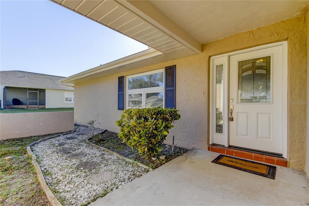 A front entryway features a white door with a glass insert and a small garden bed — 7926 FOXWOOD DRIVE, NEW PORT RICHEY, FL