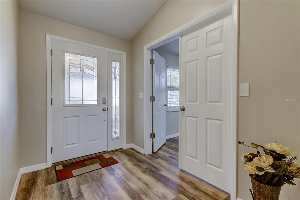 An entryway features a white front door, wood-look flooring, and an open interior door — 7926 FOXWOOD DRIVE, NEW PORT RICHEY, FL