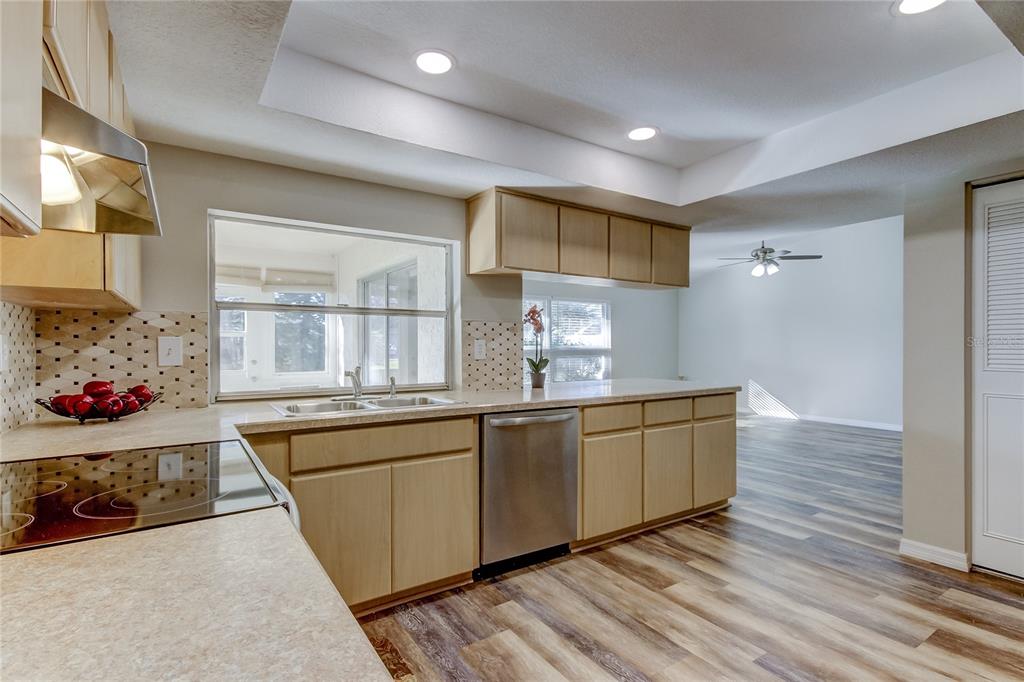 A kitchen with light wood cabinets, stainless steel dishwasher, and a window overlooking a sunroom — 7926 FOXWOOD DRIVE, NEW PORT RICHEY, FL