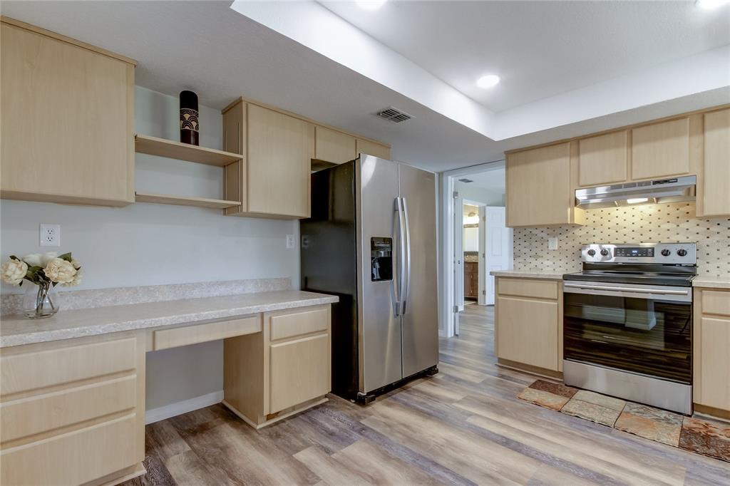 A kitchen features light wood cabinets, stainless steel appliances, and a built-in desk area — 7926 FOXWOOD DRIVE, NEW PORT RICHEY, FL