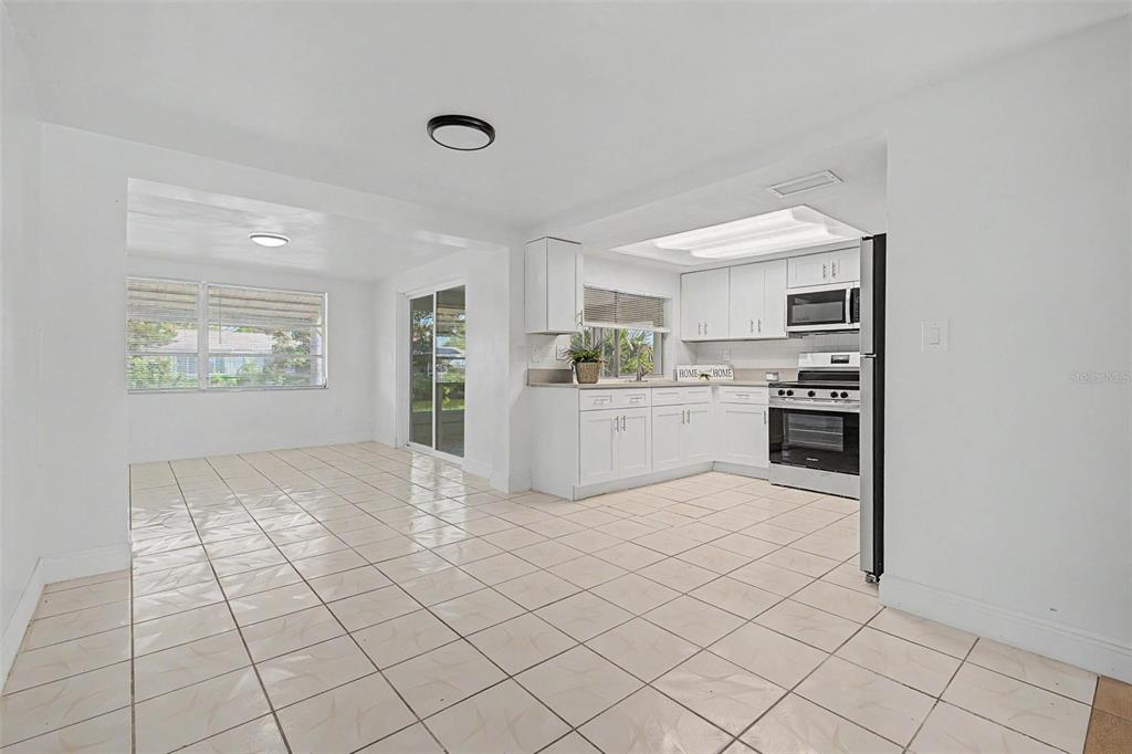 A white kitchen with tile flooring opens into a dining area with sliding glass doors — 3909 SAIL DRIVE, NEW PORT RICHEY, FL