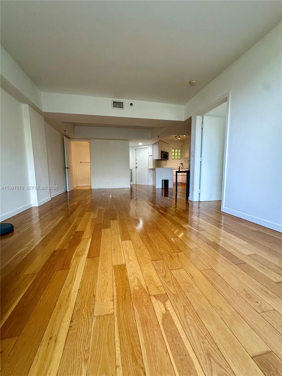 An empty living area features hardwood floors and an open kitchen in the background — 9156 Collins Ave # 202, Surfside FL 33154, SURFSIDE, FL