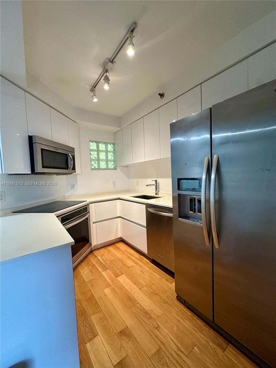 A modern kitchen features white cabinets, stainless steel appliances, and light wood flooring — 9156 Collins Ave # 202, Surfside FL 33154, SURFSIDE, FL