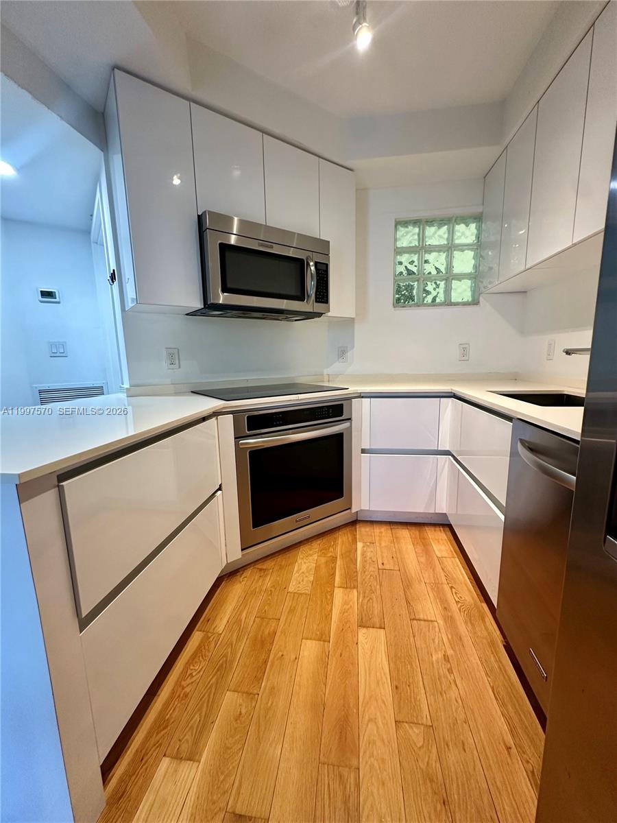 A modern kitchen features white flat-panel cabinets, stainless steel appliances, and light wood flooring — 9156 Collins Ave # 202, Surfside FL 33154, SURFSIDE, FL