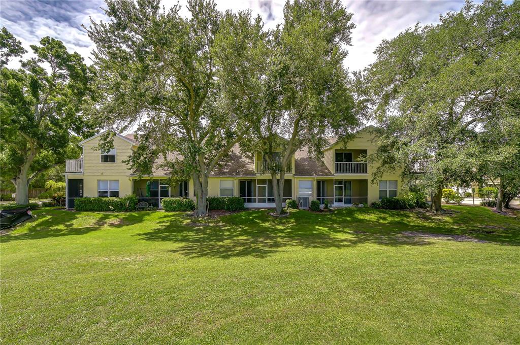 A two-story yellow apartment building sits behind a large green lawn with mature trees — 1050 STARKEY ROAD UNIT 2105, LARGO, FL