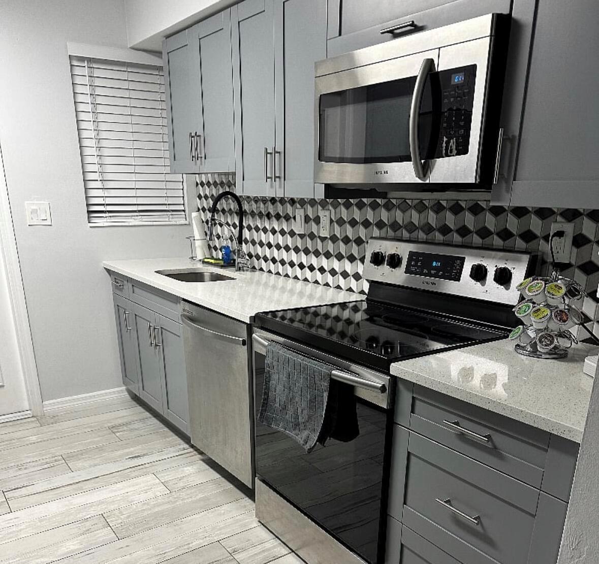 A modern kitchen features gray cabinets, stainless steel appliances, white countertops, and a geometric backsplash — 136 Akron Street # B2, FL 33461, FL