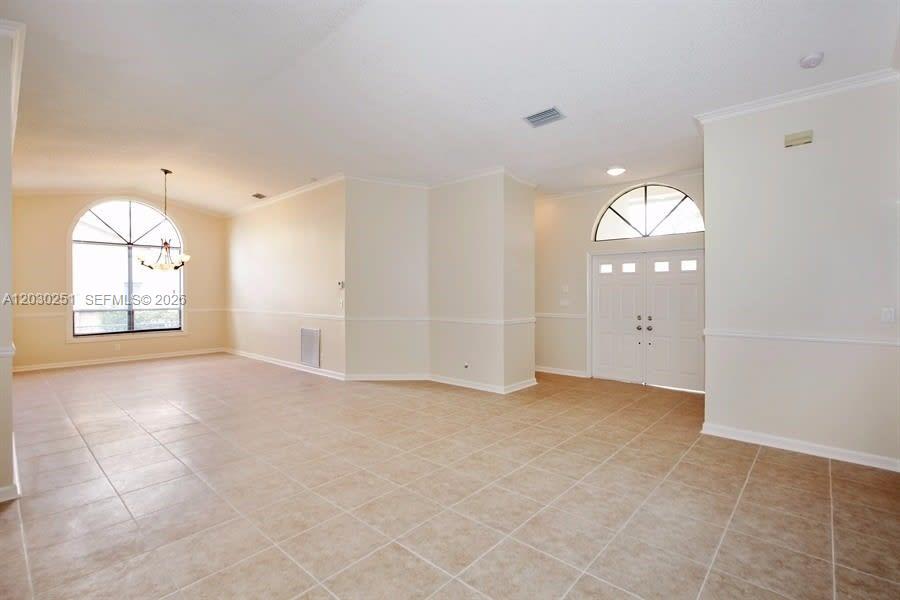 An empty room features beige tile flooring, white walls, and arched windows — CORAL SPRINGS, FL