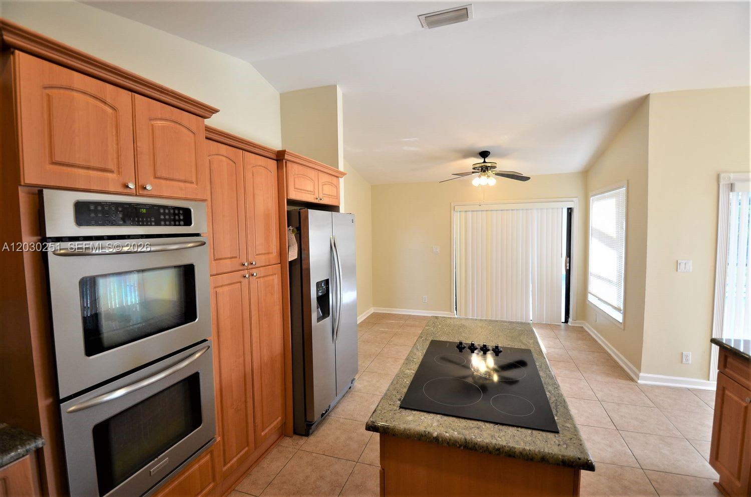 A kitchen features wood cabinets, stainless steel double ovens, a refrigerator, and a center island — CORAL SPRINGS, FL