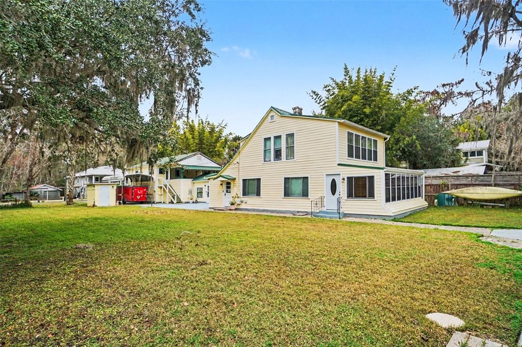 A two-story yellow house with a screened porch stands on a grassy lot with trees — 55316 CLAIRE STREET, ASTOR, FL