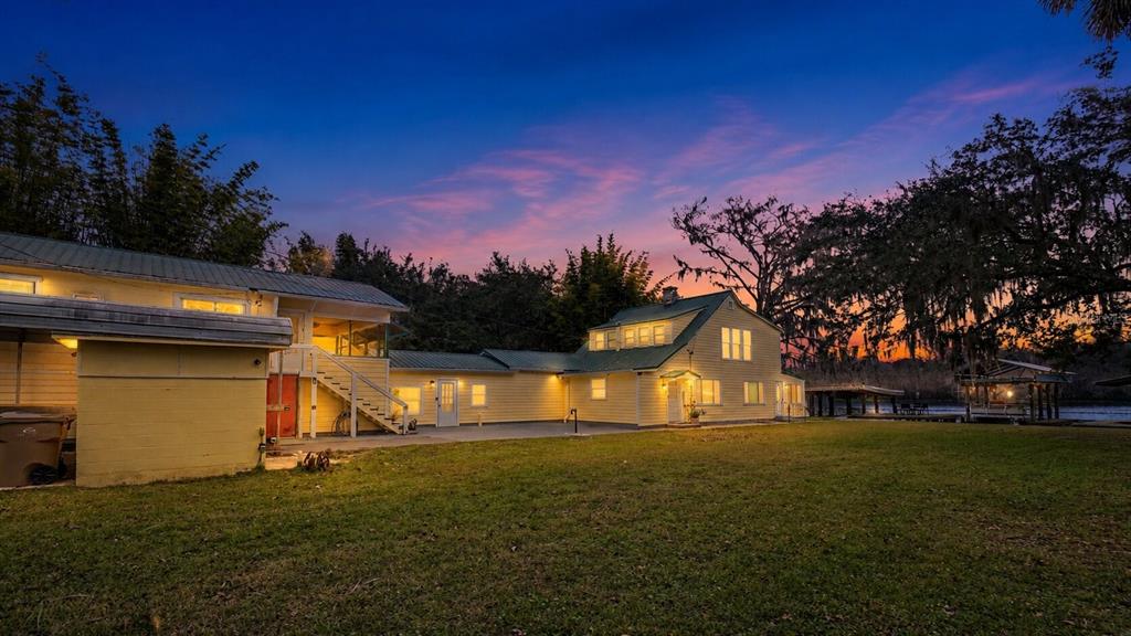 A yellow two-story house with a metal roof sits on a lawn at sunset — 55316 CLAIRE STREET, ASTOR, FL