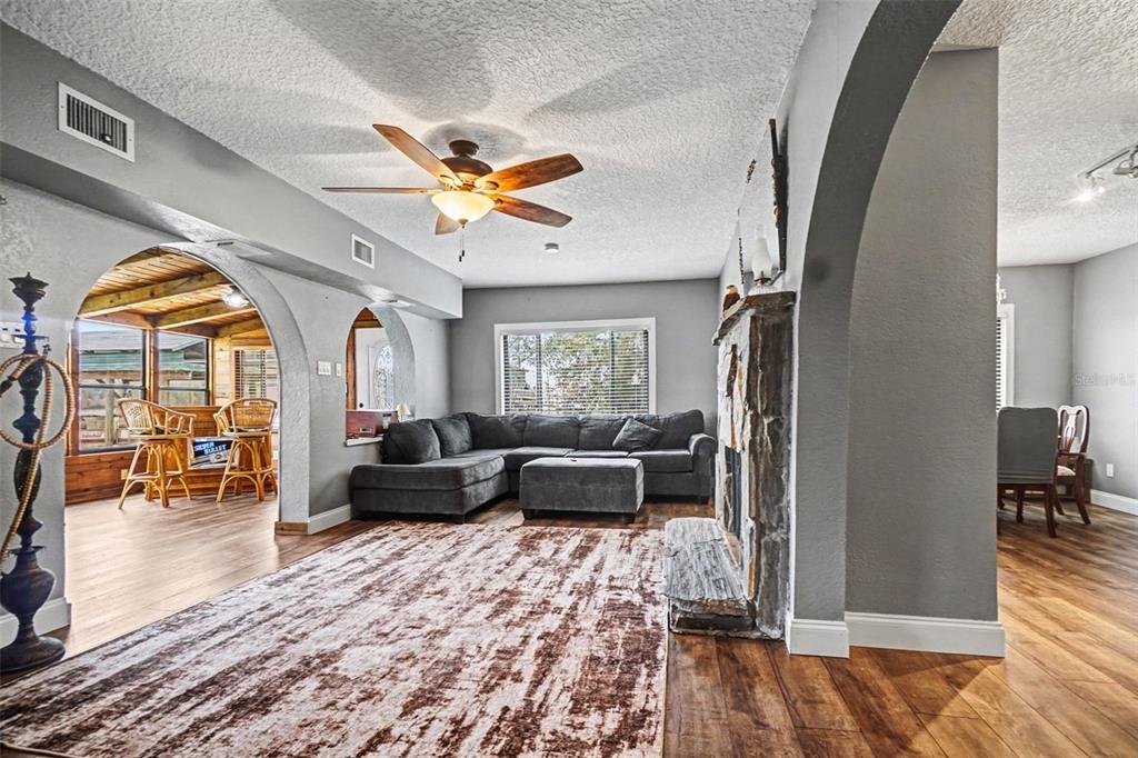 A living room features a stone fireplace, gray sectional sofa, and arched doorways leading elsewhere — 55316 CLAIRE STREET, ASTOR, FL