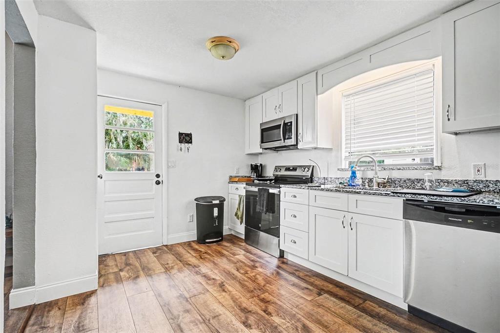 A kitchen features white cabinets, stainless steel appliances, granite countertops, and wood-look flooring — 55316 CLAIRE STREET, ASTOR, FL