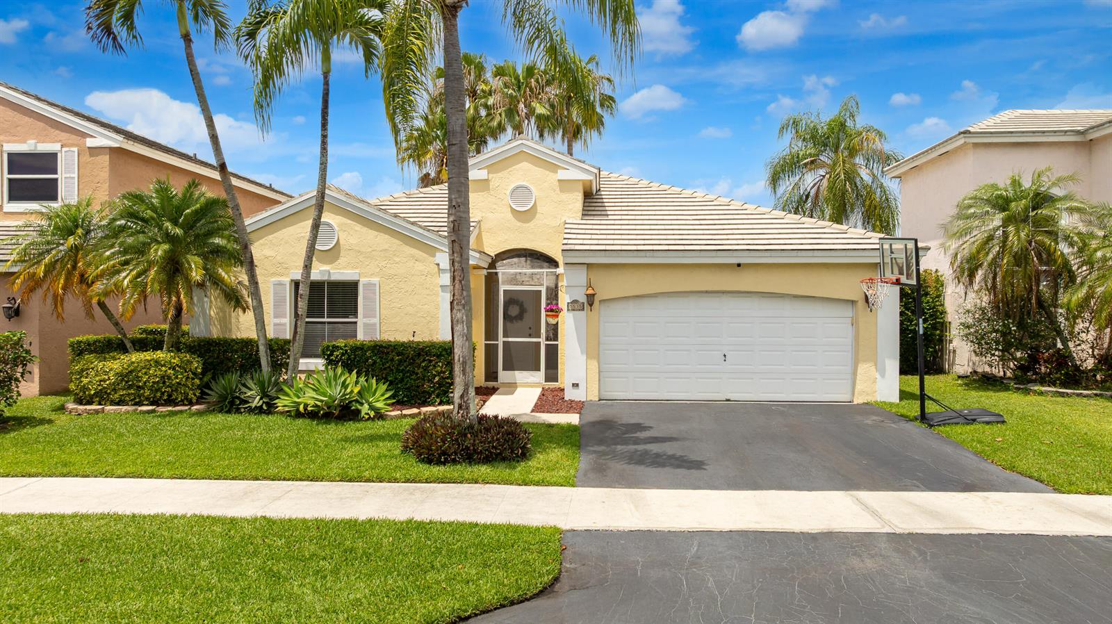 A single-story yellow house with a two-car garage, palm trees, and a basketball hoop — 5535 NW 54th Circle, Coconut Creek FL 33073, COCONUT CREEK, FL