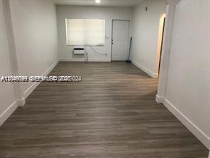 An empty room features light-colored wood-look flooring, white walls, a window unit, and a door — 30 S Shore Dr # 6, Miami Beach FL 33141, MIAMI BEACH, FL