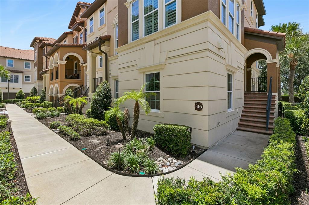 The exterior of a multi-story tan stucco townhouse features a concrete walkway and stairs — 316 TRIESTE LOOP, LAKE MARY, FL