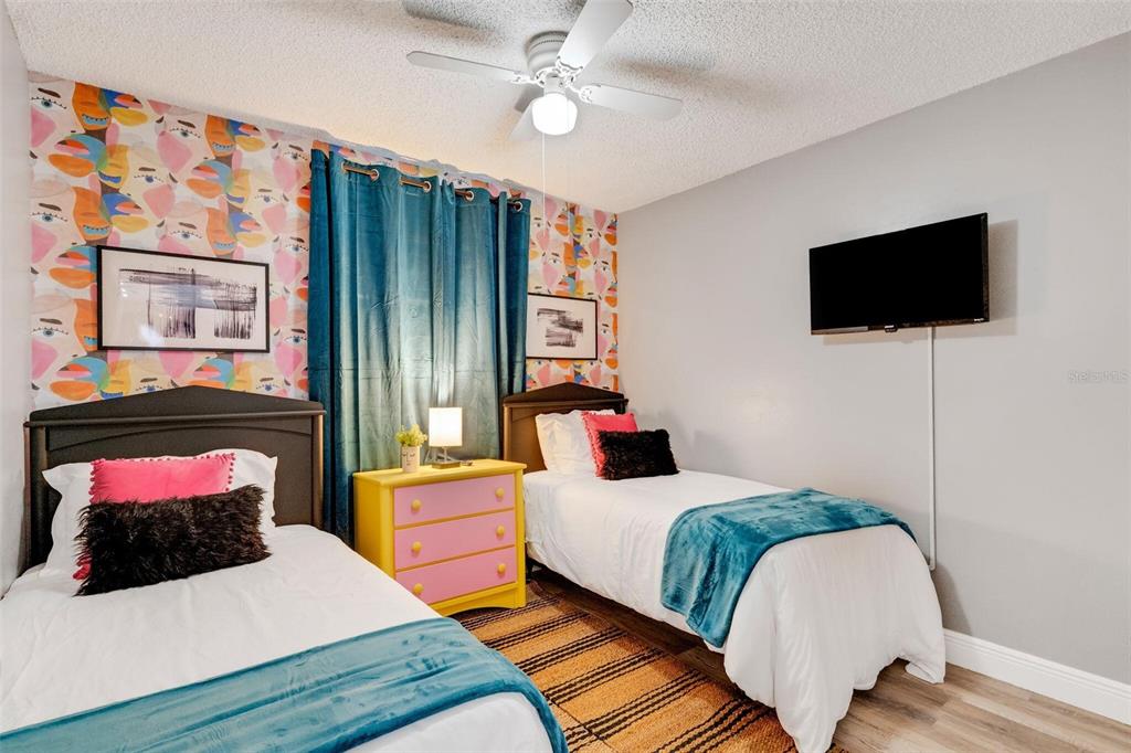 A bedroom features two twin beds, colorful patterned wallpaper, a yellow dresser, and a television — 3357 TIMBERLINE ROAD W, WINTER HAVEN, FL
