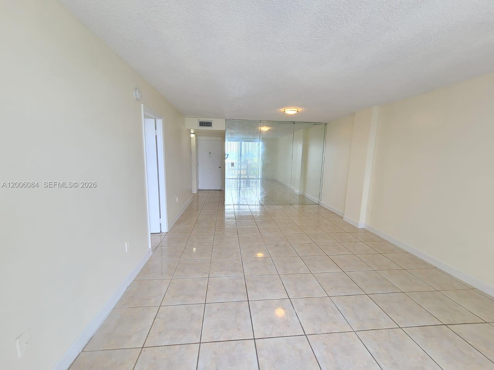 An empty room features beige tiled flooring, light-colored walls, and a mirrored accent wall — 15600 NW 7th Ave # 709, Miami FL 33169, MIAMI, FL