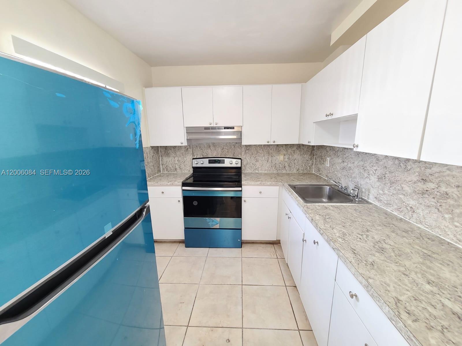 A kitchen features white cabinets, a blue refrigerator, a black stove, and gray countertops — 15600 NW 7th Ave # 709, Miami FL 33169, MIAMI, FL