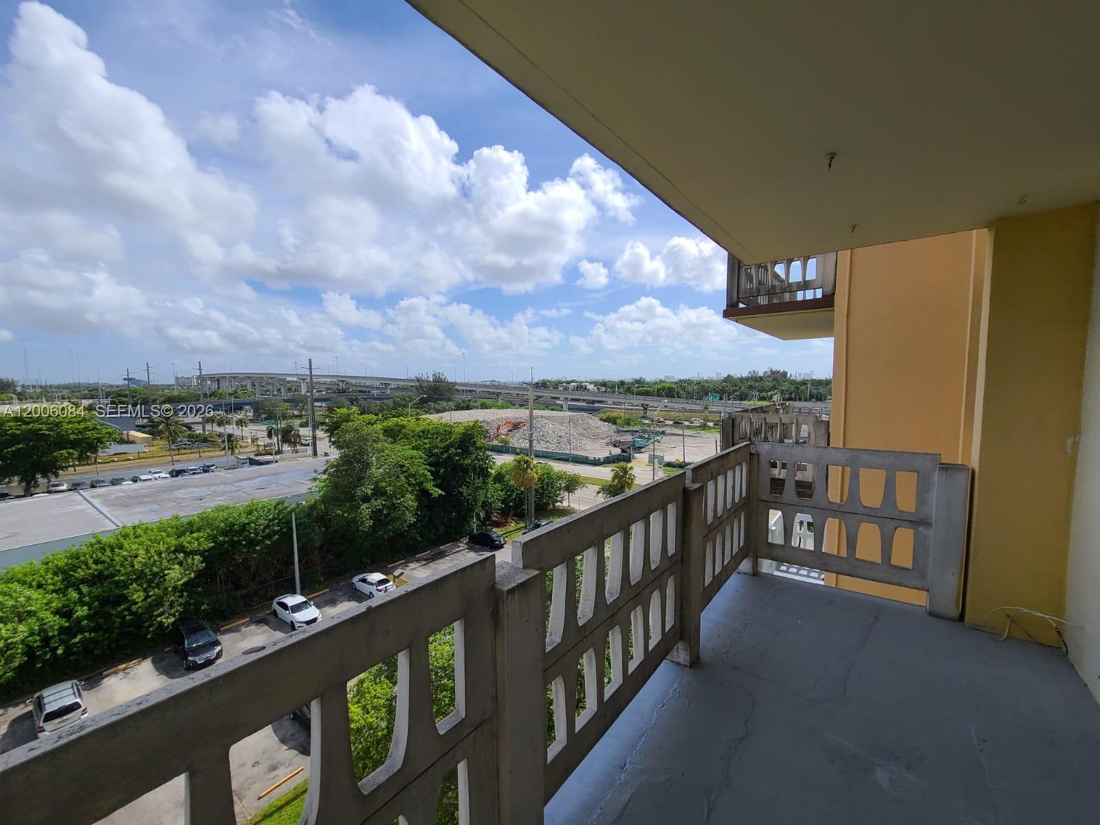 A concrete balcony overlooks a parking lot, green trees, and a distant highway overpass — 15600 NW 7th Ave # 709, Miami FL 33169, MIAMI, FL