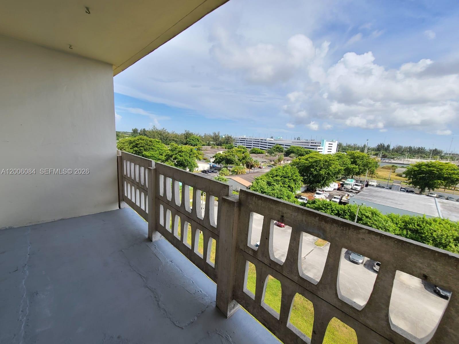 A concrete balcony overlooks a parking lot, green trees, and a distant building — 15600 NW 7th Ave # 709, Miami FL 33169, MIAMI, FL