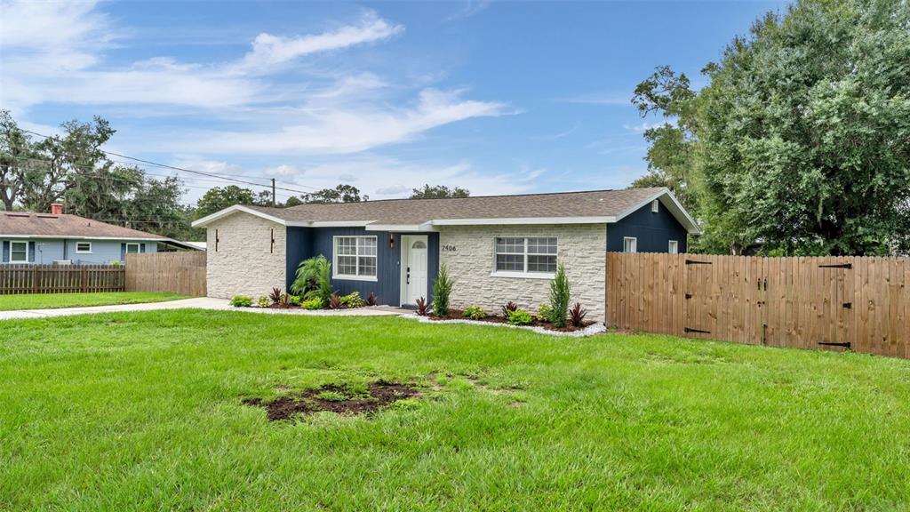 A single-story house with stone veneer and dark blue siding sits behind a wooden fence — 2406 FUTCH ROAD, LAKELAND, FL