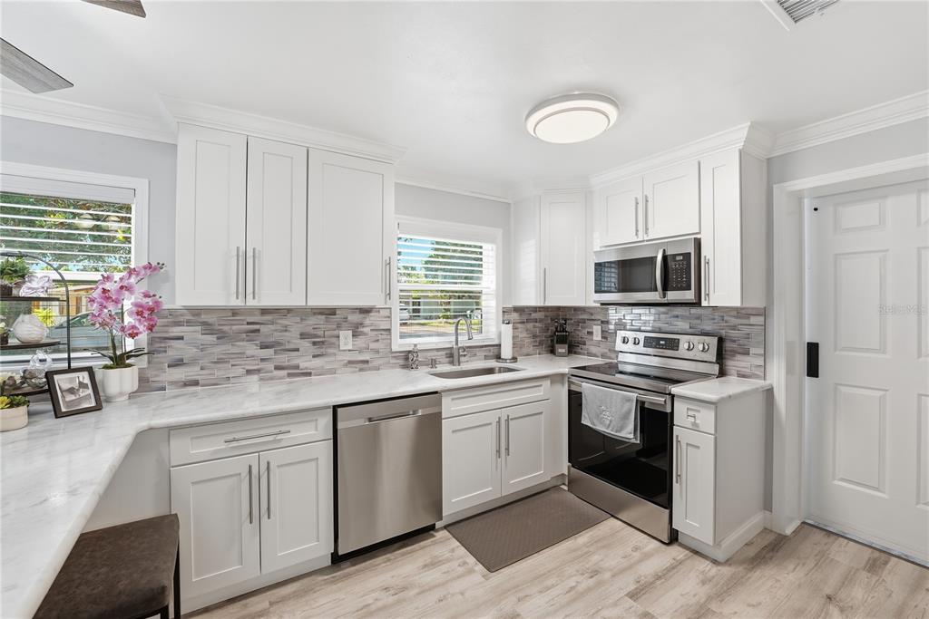 A kitchen features white cabinets, stainless steel appliances, a marble countertop, and a tiled backsplash — 240 N DEVON AVENUE, WINTER SPRINGS, FL