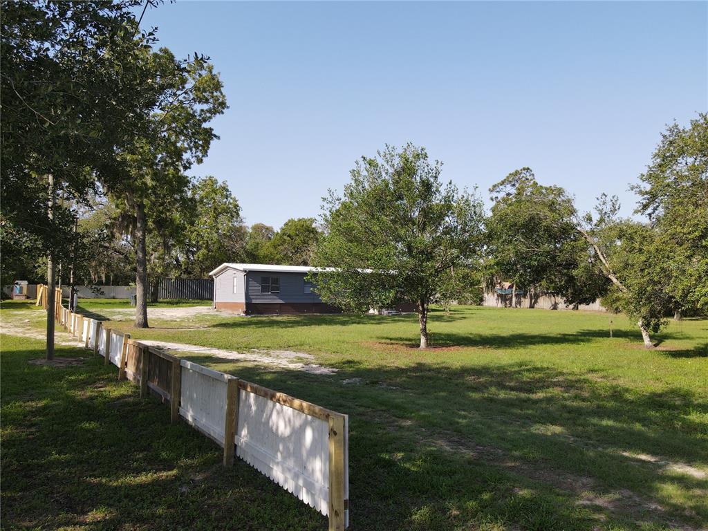 A single-story mobile home sits on a large, grassy lot enclosed by a wooden fence — 17524 MEDLEY AVENUE, SPRING HILL, FL