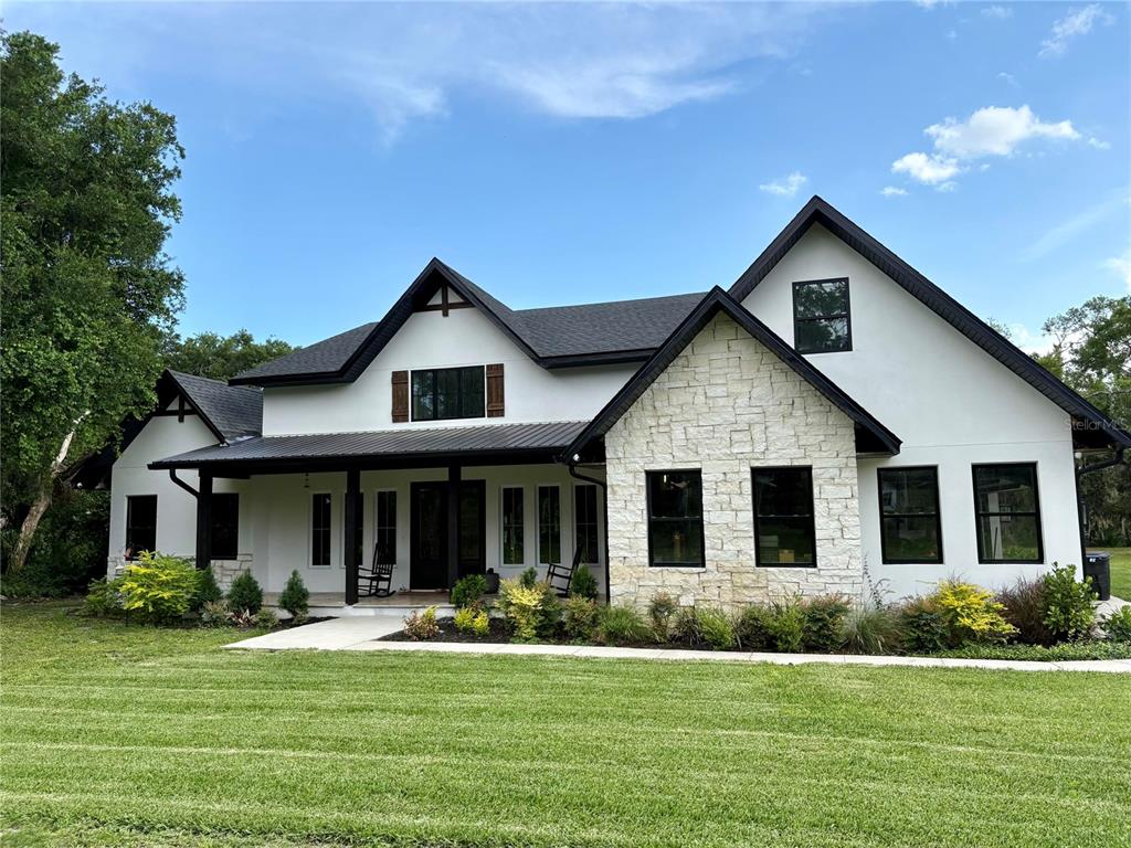 A two-story farmhouse with white stucco, stone veneer, and a black metal roof — 1781 TAYLOR ROAD, PORT ORANGE, FL