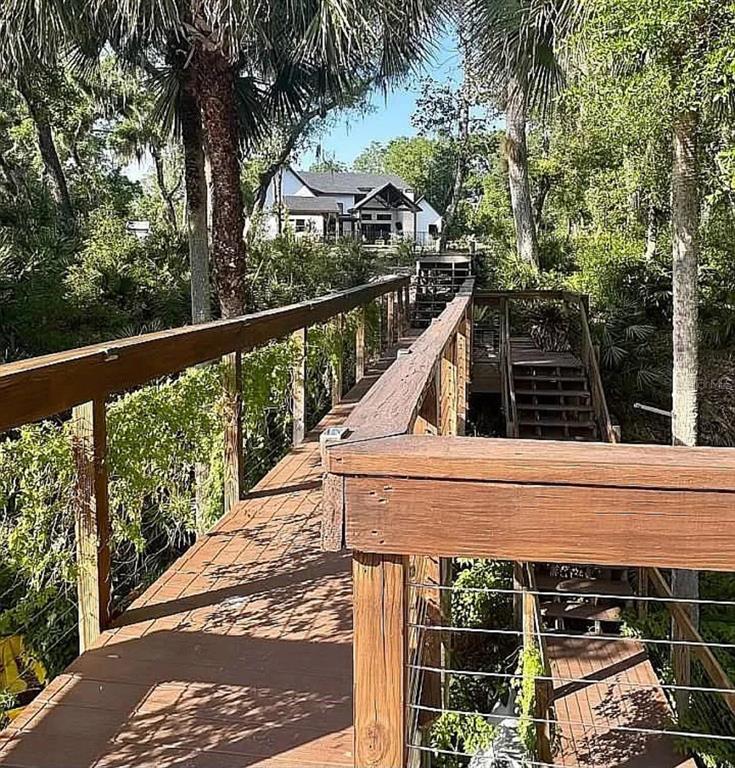 A wooden walkway with railings leads toward a house surrounded by trees and lush vegetation — 1781 TAYLOR ROAD, PORT ORANGE, FL