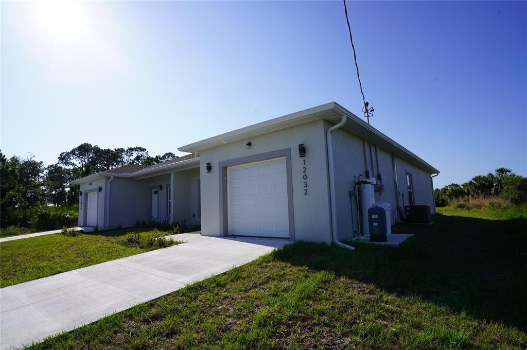 A single-story duplex with white stucco walls, two garage doors, and concrete driveways — 12032 TETZEL AVENUE, PORT CHARLOTTE, FL