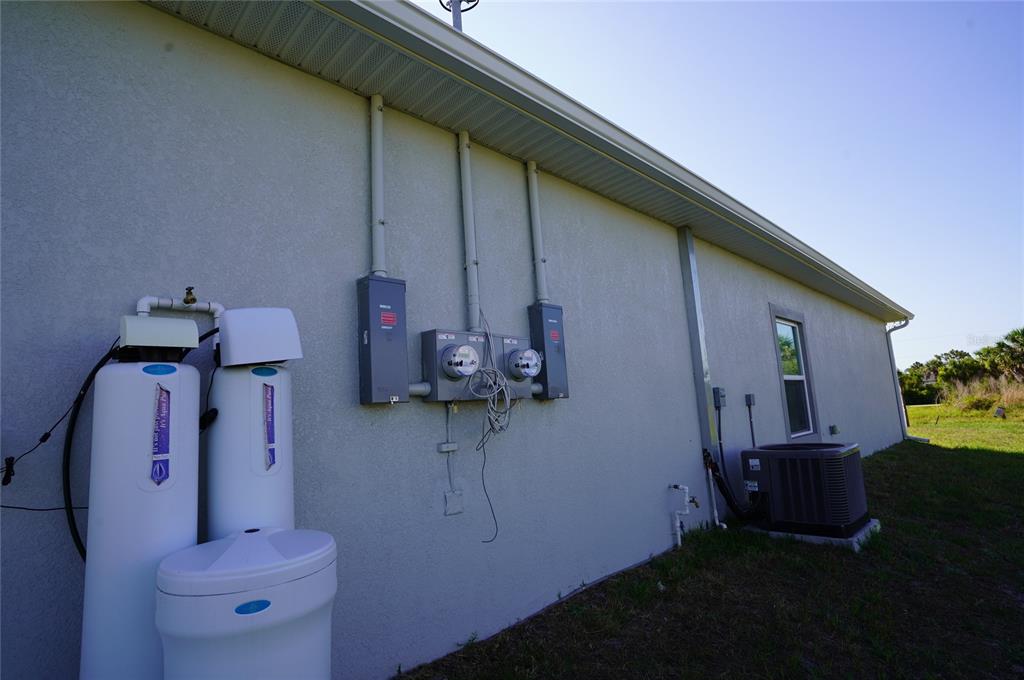 The exterior side of a house features two water treatment tanks, electrical meters, and an AC unit — 12032 TETZEL AVENUE, PORT CHARLOTTE, FL