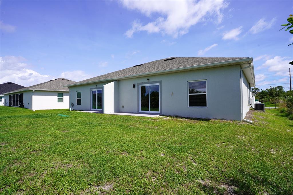 The back exterior of a light-colored stucco house features sliding glass doors and a lawn — 12032 TETZEL AVENUE, PORT CHARLOTTE, FL