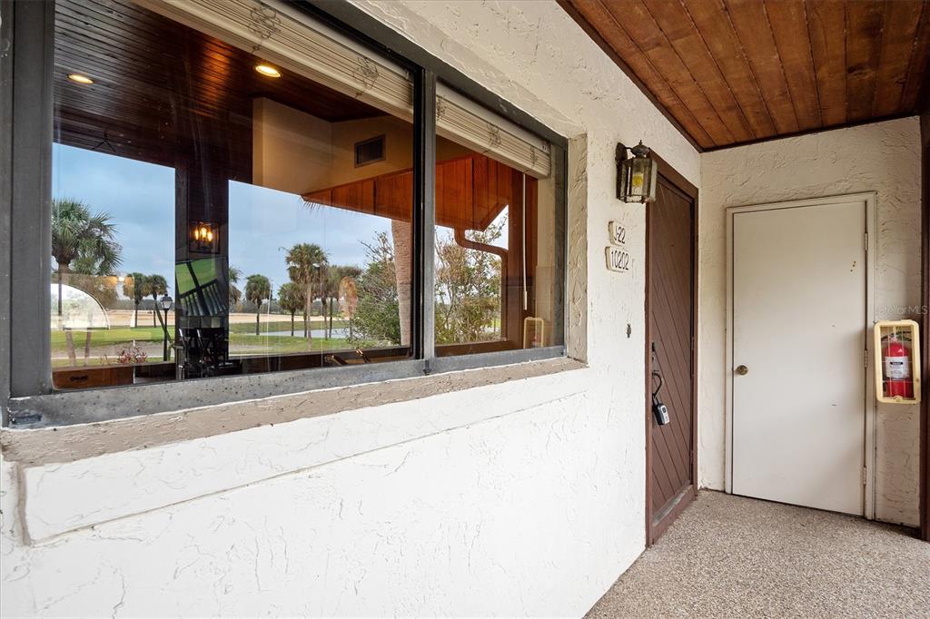 A stucco exterior wall features a large window, a dark wooden door, and a fire extinguisher — 10202 VILLAGE DRIVE UNIT 22, LAKE WALES, FL