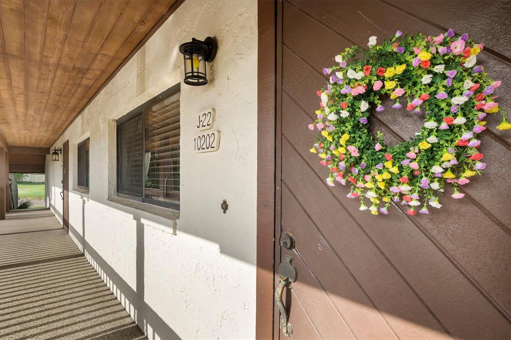 A brown front door with a floral wreath sits on a covered outdoor walkway — 10202 VILLAGE DRIVE UNIT 22, LAKE WALES, FL