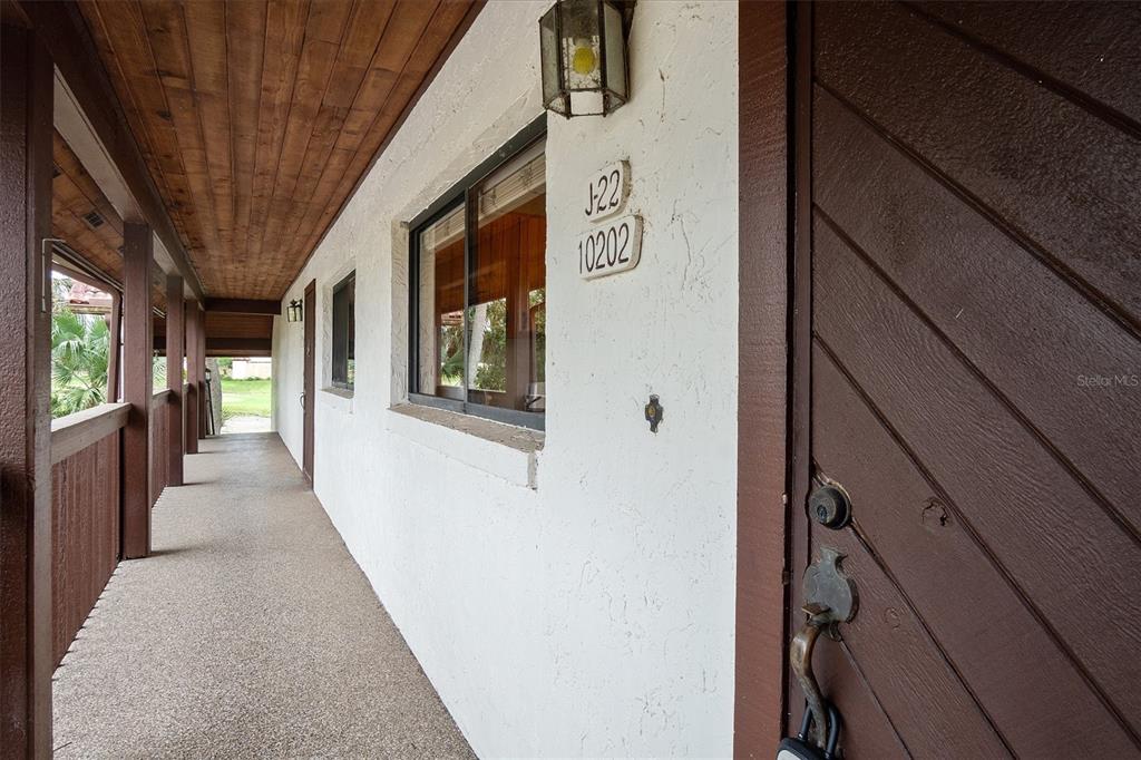 A covered exterior walkway leads to a brown door with a lockbox and unit number — 10202 VILLAGE DRIVE UNIT 22, LAKE WALES, FL
