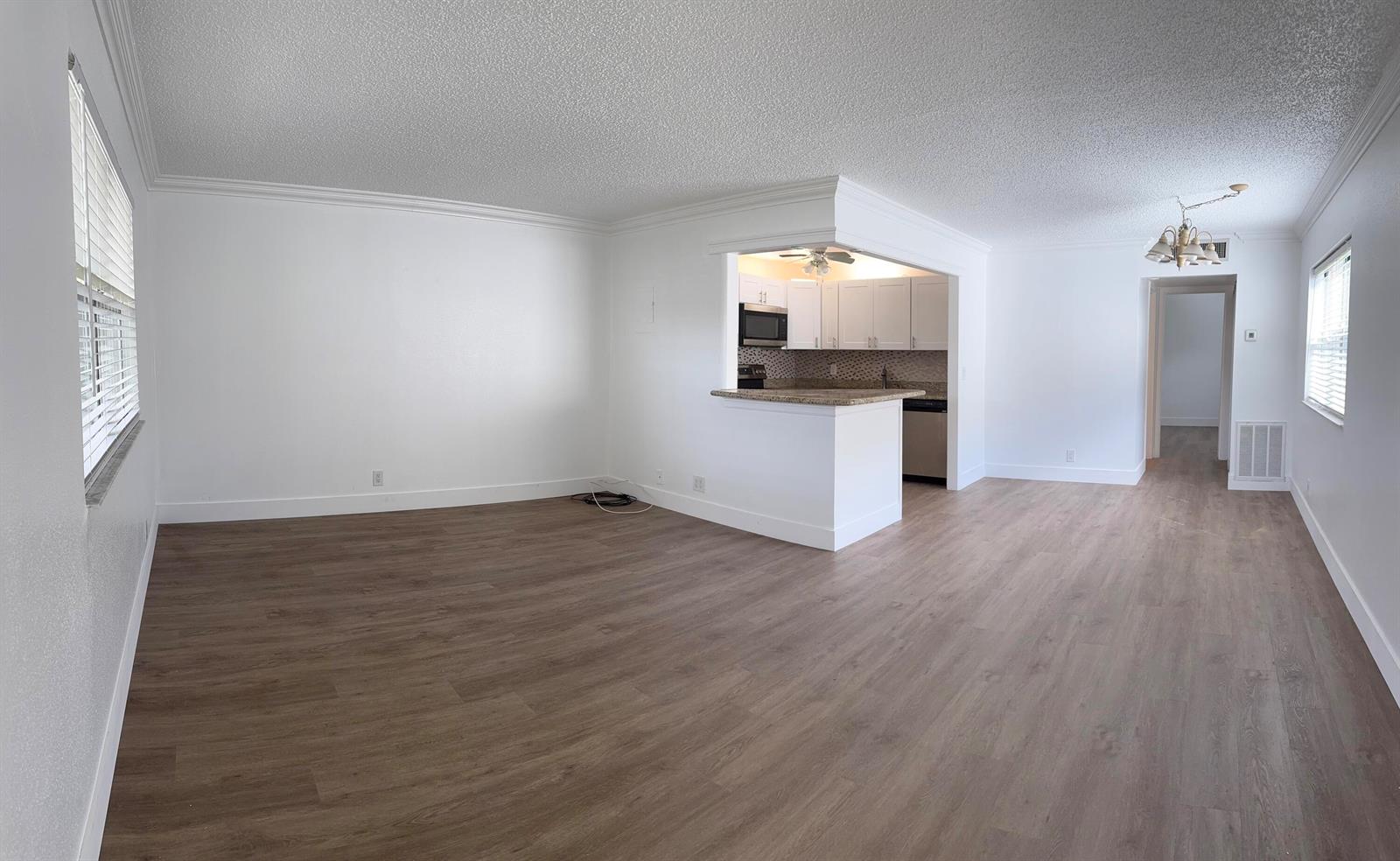 An open-concept living area features wood-look flooring, white walls, and a kitchen with a breakfast bar — 103 Saxony C, Delray Beach FL 33446, DELRAY BEACH, FL
