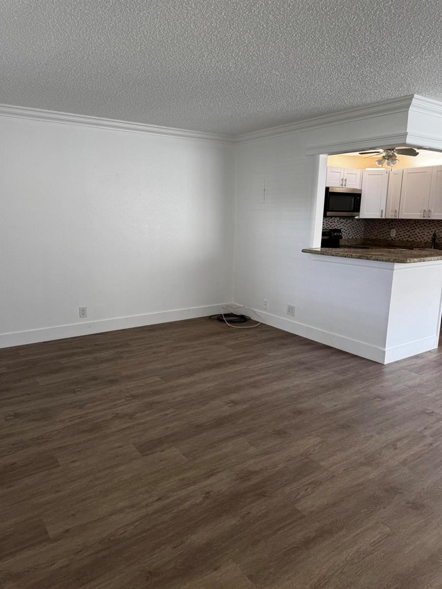 An empty living room with wood-look flooring and a pass-through opening to the kitchen — 103 Saxony C, Delray Beach FL 33446, DELRAY BEACH, FL