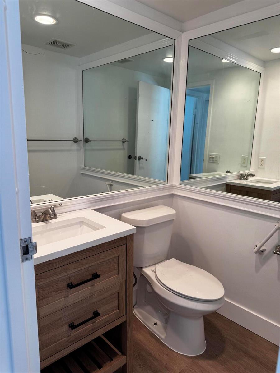 A bathroom features a wood vanity, white toilet, and large corner mirrors above the sink — 103 Saxony C, Delray Beach FL 33446, DELRAY BEACH, FL
