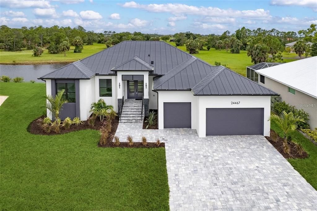 A modern single-story house with a dark metal roof, white stucco walls, and a paver driveway — 24375 BELIZE COURT, PUNTA GORDA, FL