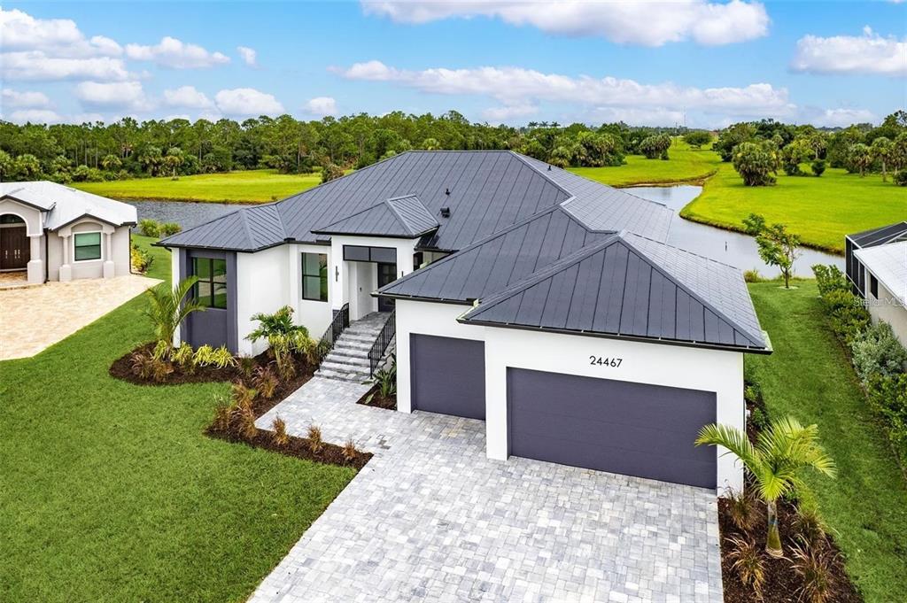 A modern single-story house with a metal roof, white stucco walls, and a paved driveway — 24375 BELIZE COURT, PUNTA GORDA, FL