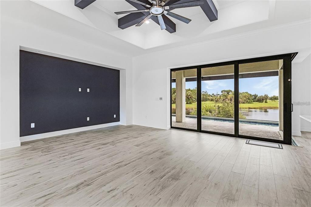 A living room features a dark accent wall, wood-look tile flooring, and large sliding glass doors — 24375 BELIZE COURT, PUNTA GORDA, FL