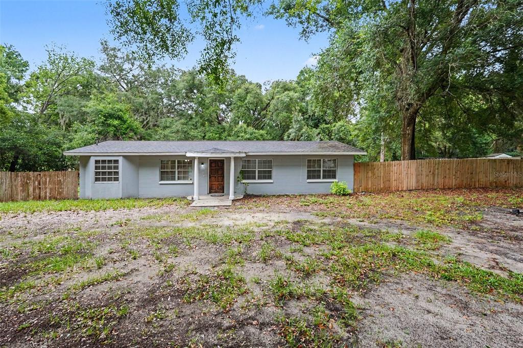 A single-story gray house with a wooden front door and a large dirt yard — 5328 LANTANA STREET, ZEPHYRHILLS, FL