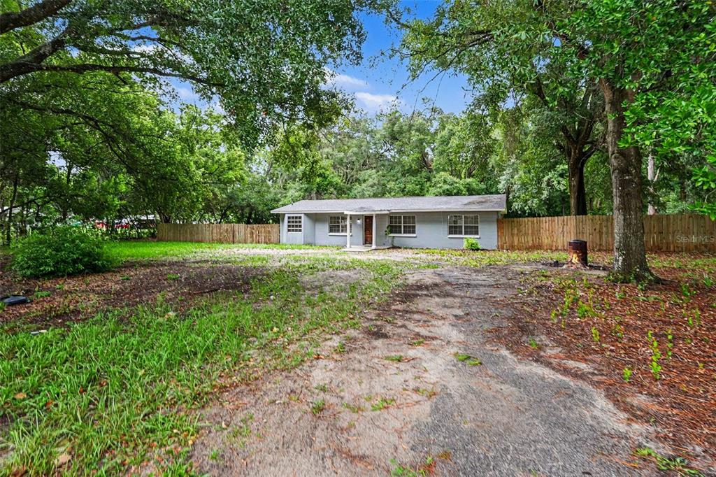 A single-story gray house sits on a large, grassy lot surrounded by mature trees — 5328 LANTANA STREET, ZEPHYRHILLS, FL